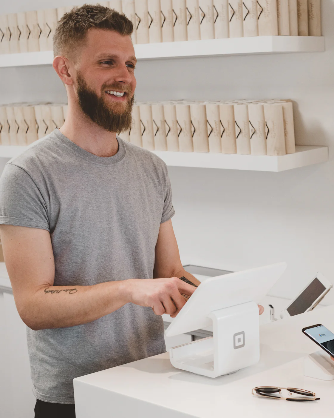 The owner of a small shop smiling behind the counter as they take a card payment on a tablet till.